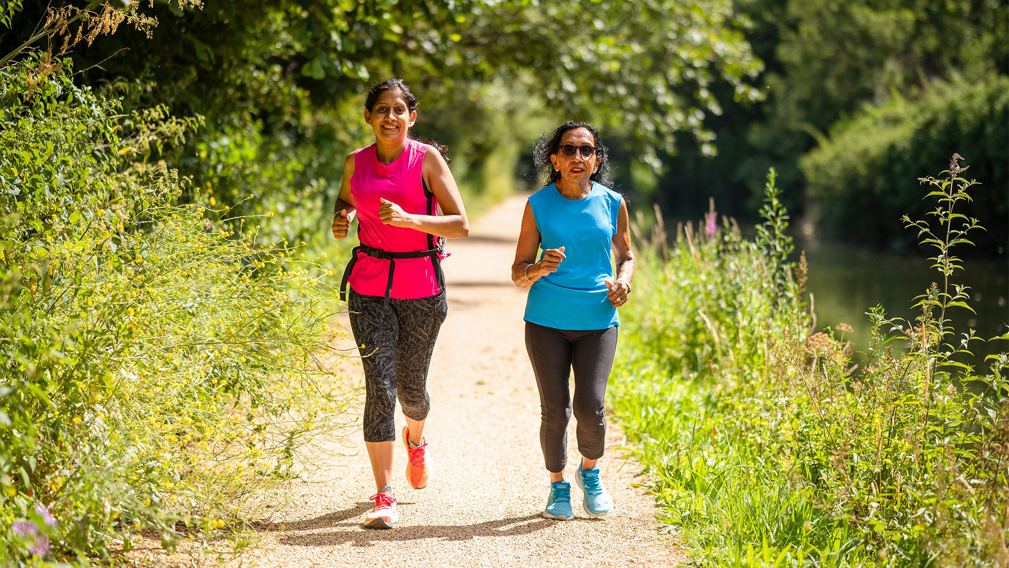 Two women running along a canal towpath in the sunshine